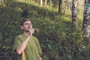 Üfleme sabun köpüğü genç adam. Yarış yaz ormandaki adam