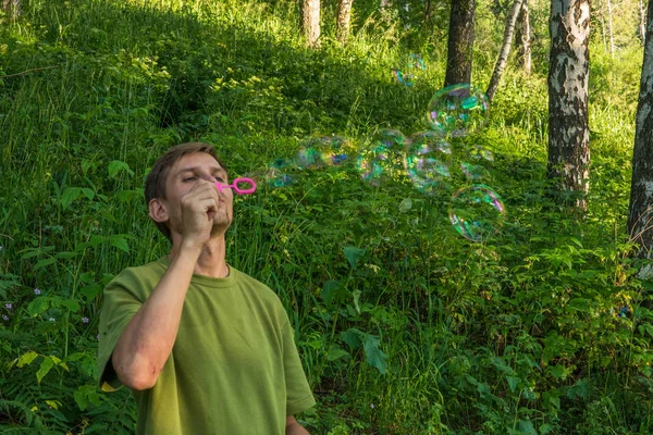 Young man blowing soap bubbles. Man in summer forest in the moun