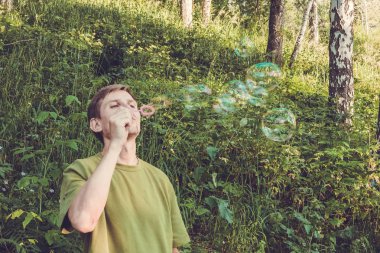 Üfleme sabun köpüğü genç adam. Yarış yaz ormandaki adam