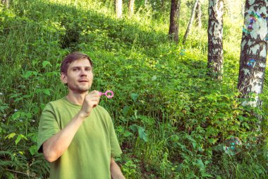 Üfleme sabun köpüğü genç adam. Yarış yaz ormandaki adam