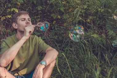 Üfleme sabun köpüğü genç adam. Yarış yaz ormandaki adam