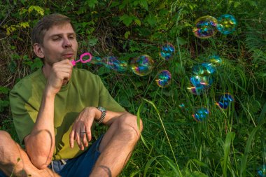 Üfleme sabun köpüğü genç adam. Yarış yaz ormandaki adam