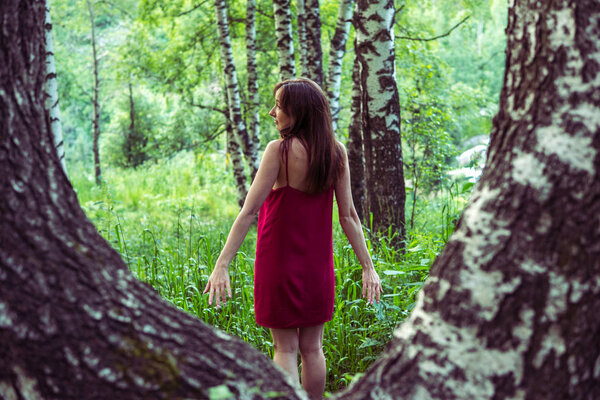 Pretty girl in red dress in a summer forest in the mountains.
