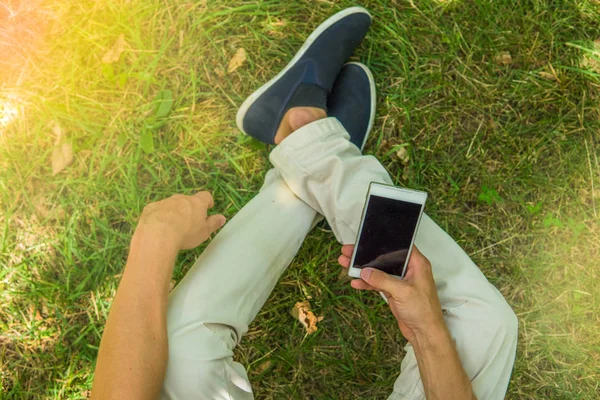 Bacaklar ve cep telefonu üst görüntüleyin. Onun smartphone oturan adam 