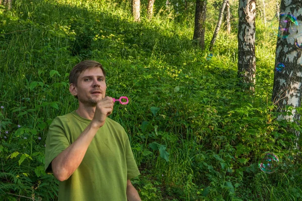 Young man blowing soap bubbles. Man in summer forest in the moun