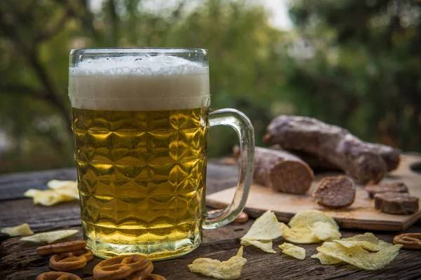 Пиво, сосиски и крендельки на деревянной доске на открытом воздухе. Октябрь — стоковое фото