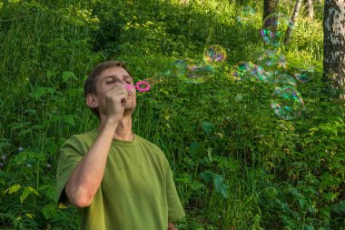 Üfleme sabun köpüğü genç adam. Yarış yaz ormandaki adam