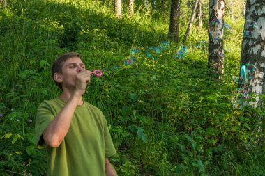Üfleme sabun köpüğü genç adam. Yarış yaz ormandaki adam