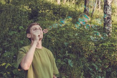 Üfleme sabun köpüğü genç adam. Yarış yaz ormandaki adam