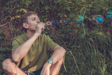 Üfleme sabun köpüğü genç adam. Yarış yaz ormandaki adam