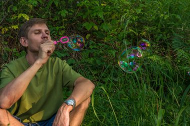 Üfleme sabun köpüğü genç adam. Yarış yaz ormandaki adam