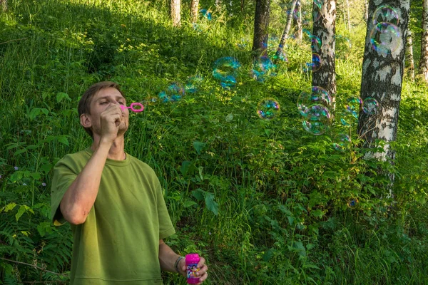 Üfleme sabun köpüğü genç adam. Yarış yaz ormandaki adam
