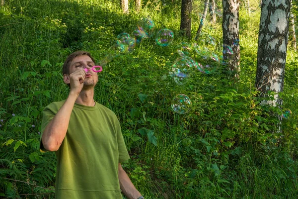Üfleme sabun köpüğü genç adam. Yarış yaz ormandaki adam