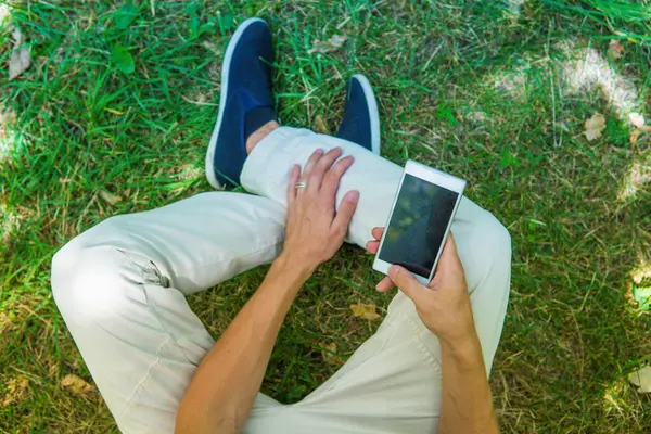 Bacaklar ve cep telefonu üst görüntüleyin. Onun smartphone oturan adam 