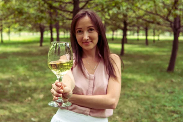 Mladá žena s bílým vínem v parku — Stock fotografie