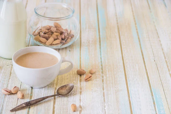Káva s mlékem a pistácie na dřevěný stůl, kopie prostor — Stock fotografie