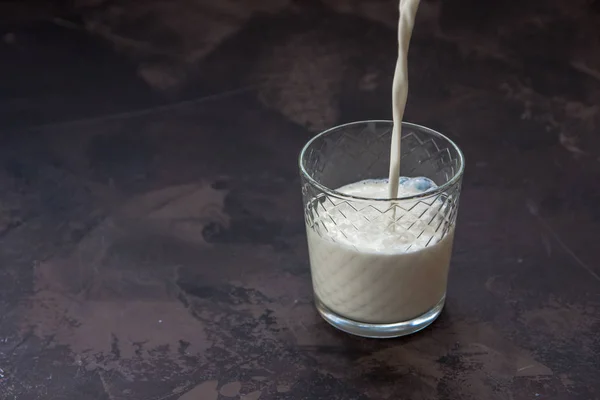 Melk gieten in een glas, donkere achtergrond — Stockfoto