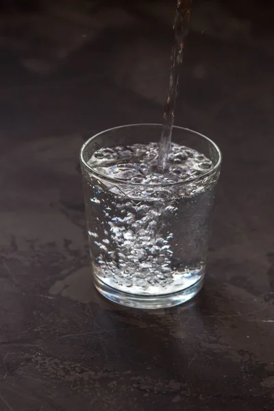 Water pouring into a glass, dark background — Stock Photo, Image