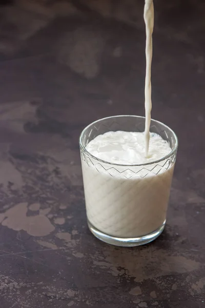 Milk pouring into a glass, dark background — Stock Photo, Image