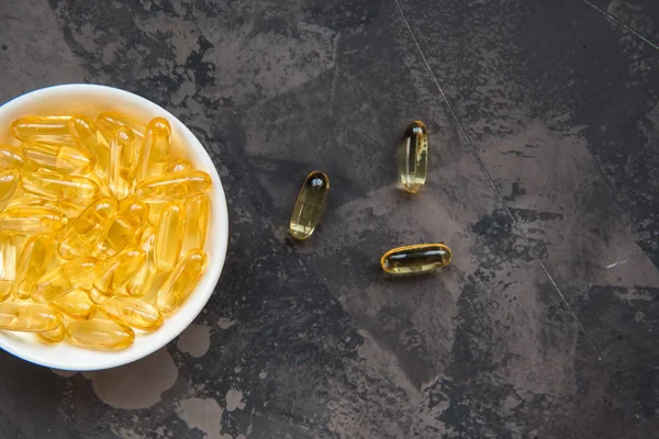 Yellow vitamin capsules on a dark background, soft gelatin capsu