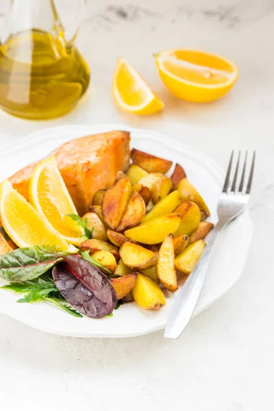 Жареный картофель с рыбой и зеленым салатом на белой тарелке — стоковое фото