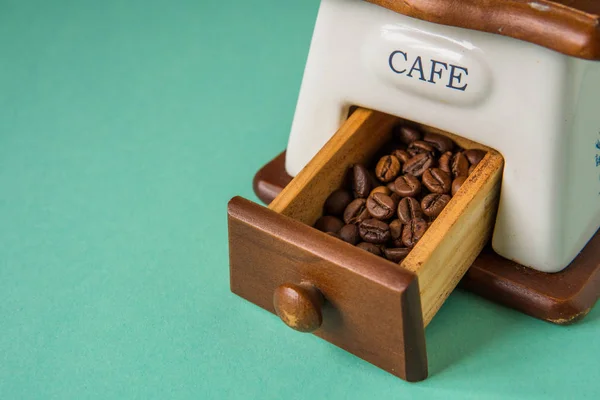 Chicchi di caffè in un macinino da caffè portatile su un tenero bac verde — Foto Stock