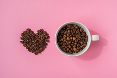 Kahve çekirdekleri kalpleri ve pembe bir arka plan üzerinde beyaz fincan şeklinde. L