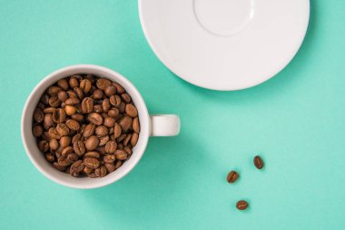 Kahve çekirdekleri bir turkuaz arka plan üzerine beyaz Kupası'nda göster.