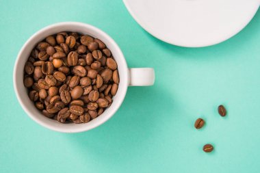Kahve çekirdekleri bir turkuaz arka plan üzerine beyaz Kupası'nda göster.