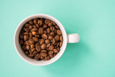 Kahve çekirdekleri bir turkuaz arka plan üzerine beyaz Kupası'nda göster.