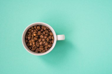 Kahve çekirdekleri bir turkuaz arka plan üzerine beyaz Kupası'nda göster.