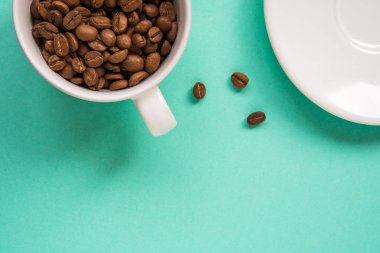 Kahve çekirdekleri bir turkuaz arka plan üzerine beyaz Kupası'nda göster.