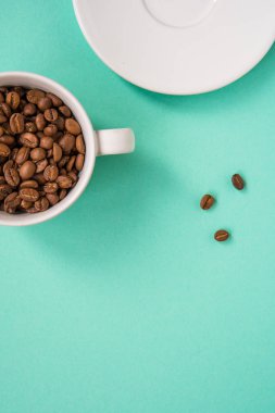 Kahve çekirdekleri bir turkuaz arka plan üzerine beyaz Kupası'nda göster.