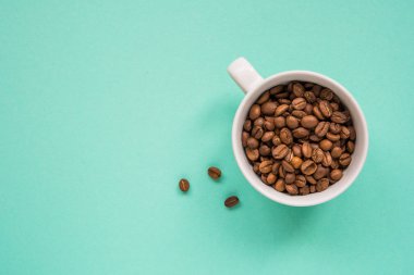 Kahve çekirdekleri bir turkuaz arka plan üzerine beyaz Kupası'nda göster.