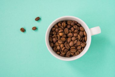 Kahve çekirdekleri bir turkuaz arka plan üzerine beyaz Kupası'nda göster.