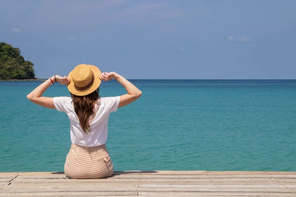 Young woman in a hat sits on a pier near the clear turquoise sea — Stock Photo, Image