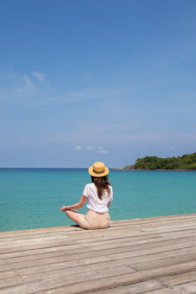 Young woman in a hat sits on a pier near the clear turquoise sea — Stock Photo, Image