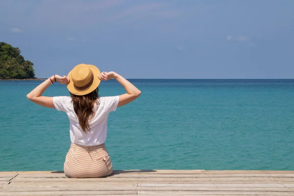 모자를 쓴 젊은 여자맑은 청록색 바다 근처 부두에 앉아 있다 로열티 프리 스톡 사진