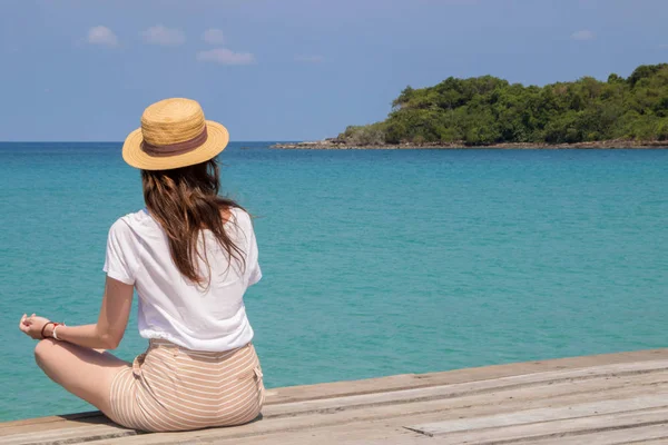 Young woman in a hat sits on a pier near the clear turquoise sea — Stock Photo, Image