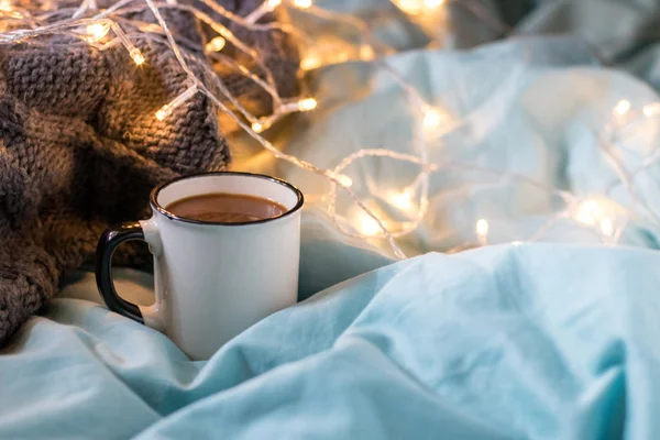 Coffee cup and garland on a bed. Atmospheric hygge style. Cozy w — Stock Photo, Image