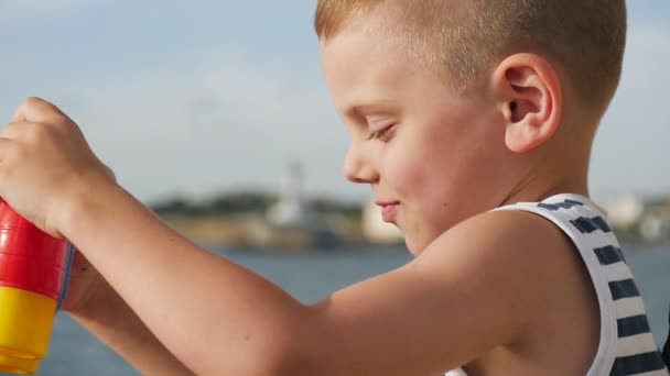 Little boy in a striped shirt holding a pair of binoculars in front of the sea — Stock Video