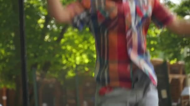 Милый малыш в клетчатой рубашке прыгает на батуте — стоковое видео
