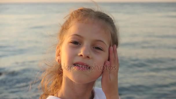 Adorable niña en un fondo de mar puesta de sol muestra e inflar sus labios — Vídeos de Stock