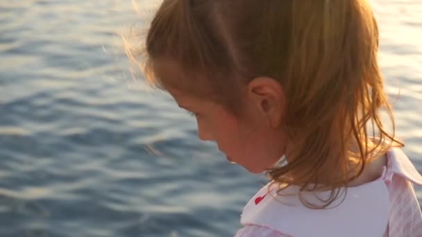 Красива маленька дівчинка біля моря на заході сонця — стокове відео
