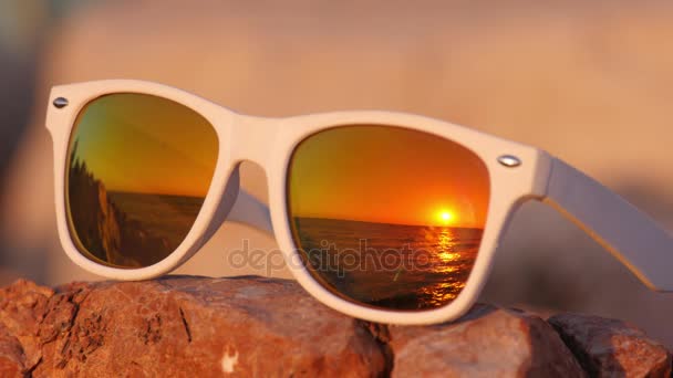 Puesta de sol en el océano reflejada en gafas de sol sobre la piedra — Vídeos de Stock