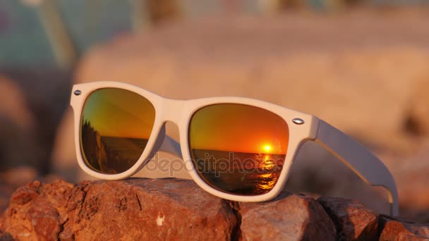 Puesta de sol idílica reflejada en gafas de sol acostadas en la piedra — Vídeos de Stock