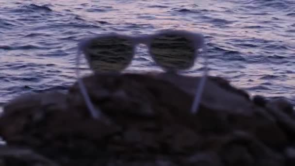Okulary przeciwsłoneczne leżą na kamieniu na tle morza — Wideo stockowe