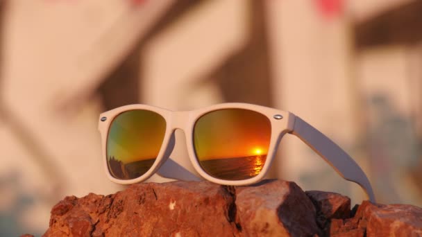 Puesta de sol de mar reflejada en gafas de sol acostadas en la piedra — Vídeo de stock