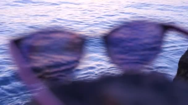 Modne okulary przeciwsłoneczne leżą na kamieniu na tle morza — Wideo stockowe