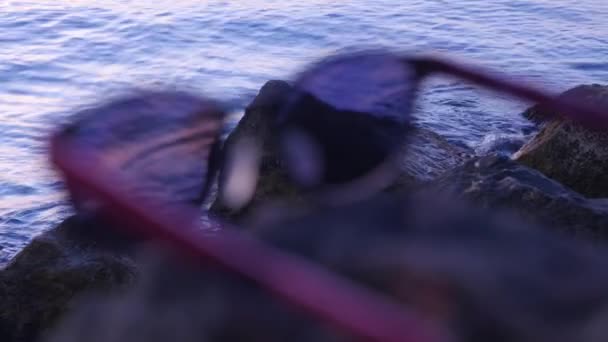 Modieuze zonnebrillen liggen op een steen op de achtergrond van de zee — Stockvideo